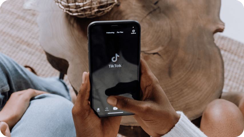 Hands holding a smartphone showing the TikTok app open on its loading screen.