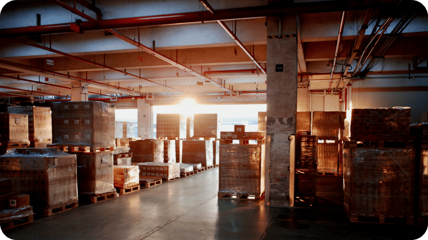 Warehouse aisle lined with shrink-wrapped pallets of stock, lit by evening sun