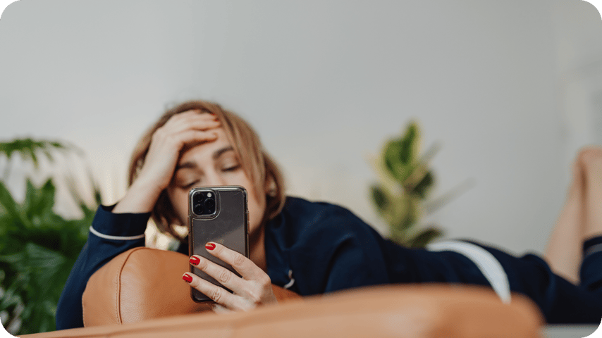 now this one:  A woman lies back with her hand on her forehead in a stressed or tired expression while looking at her phone.