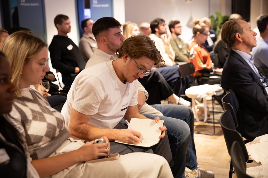 Audience seated in rows at Capsule’s B-Corp 30 event. One person in the foreground is writing notes in a notebook while others listen attentively.