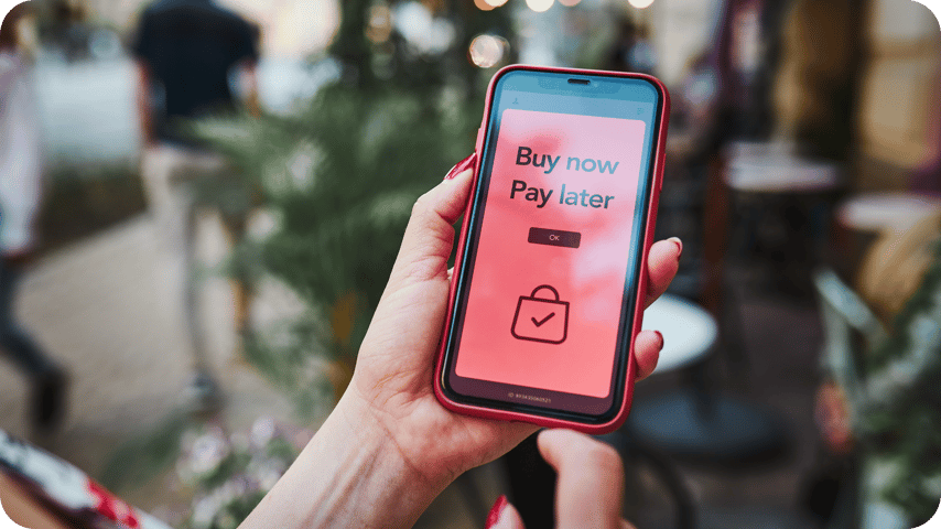 A person holding a smartphone displaying a 'Buy Now Pay Later' app screen with a shopping bag icon"