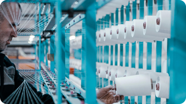 Worker examining thread spools on a blue industrial rack in a textile factor