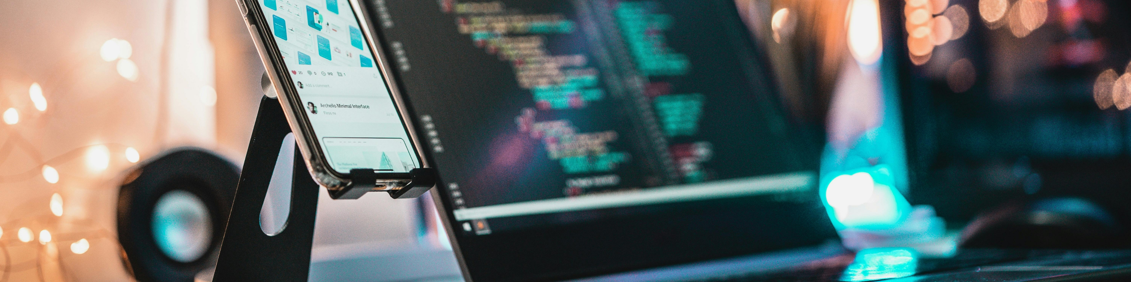 Close-up of a laptop screen displaying lines of code in a development environment, with a blurred background of warm lights and a desk setup, suggesting a modern tech or software development workspace.